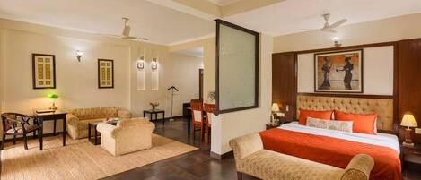 Habitación de hotel con cama, dos sofás, escritorio, silla, televisor y un cuadro en la pared.