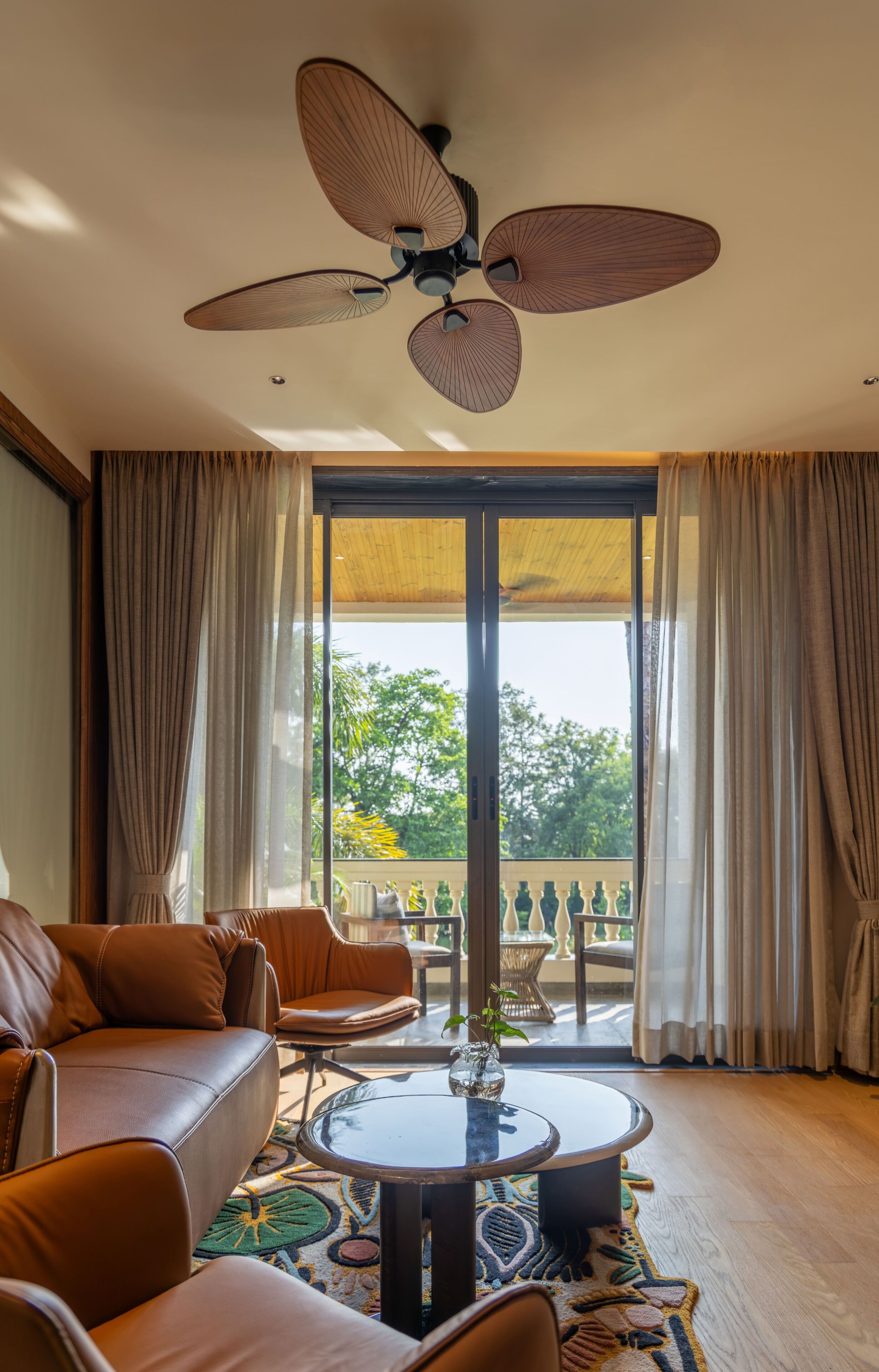 A living room with a ceiling fan, leather sofa, round coffee table, and a view through large glass doors.