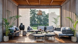 Un espace extérieur moderne, aménagé pour se détendre, avec un sol en bois, divers types de sièges, notamment des canapés et des fauteuils, et des plantes en pot.