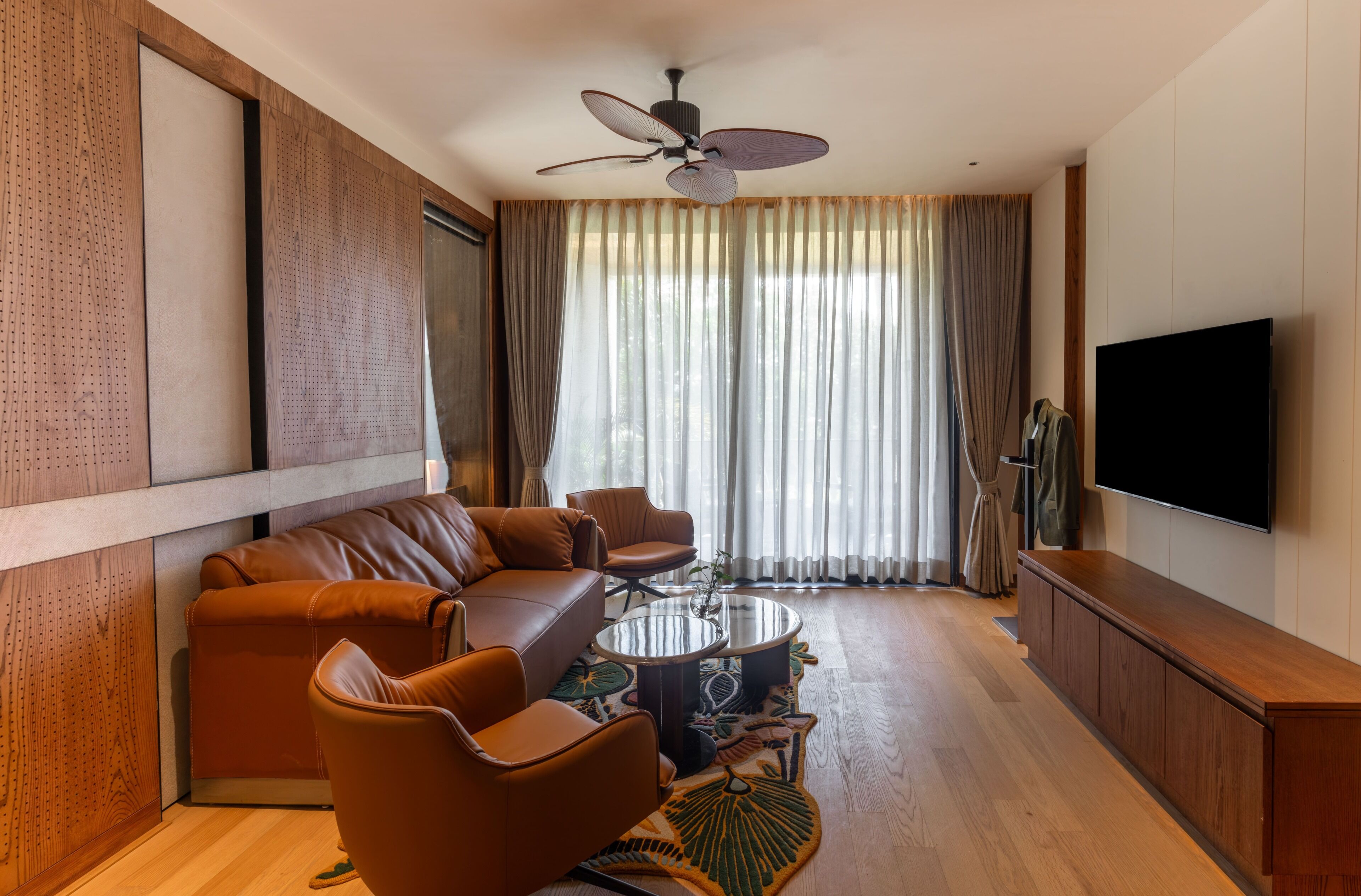 A modern living room with a sectional sofa, a round coffee table, a ceiling fan, and a flat-screen TV.