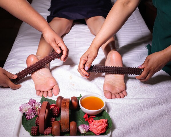Een massage met een voetmassageapparaat, een kom olie en houten voorwerpen op een bed.