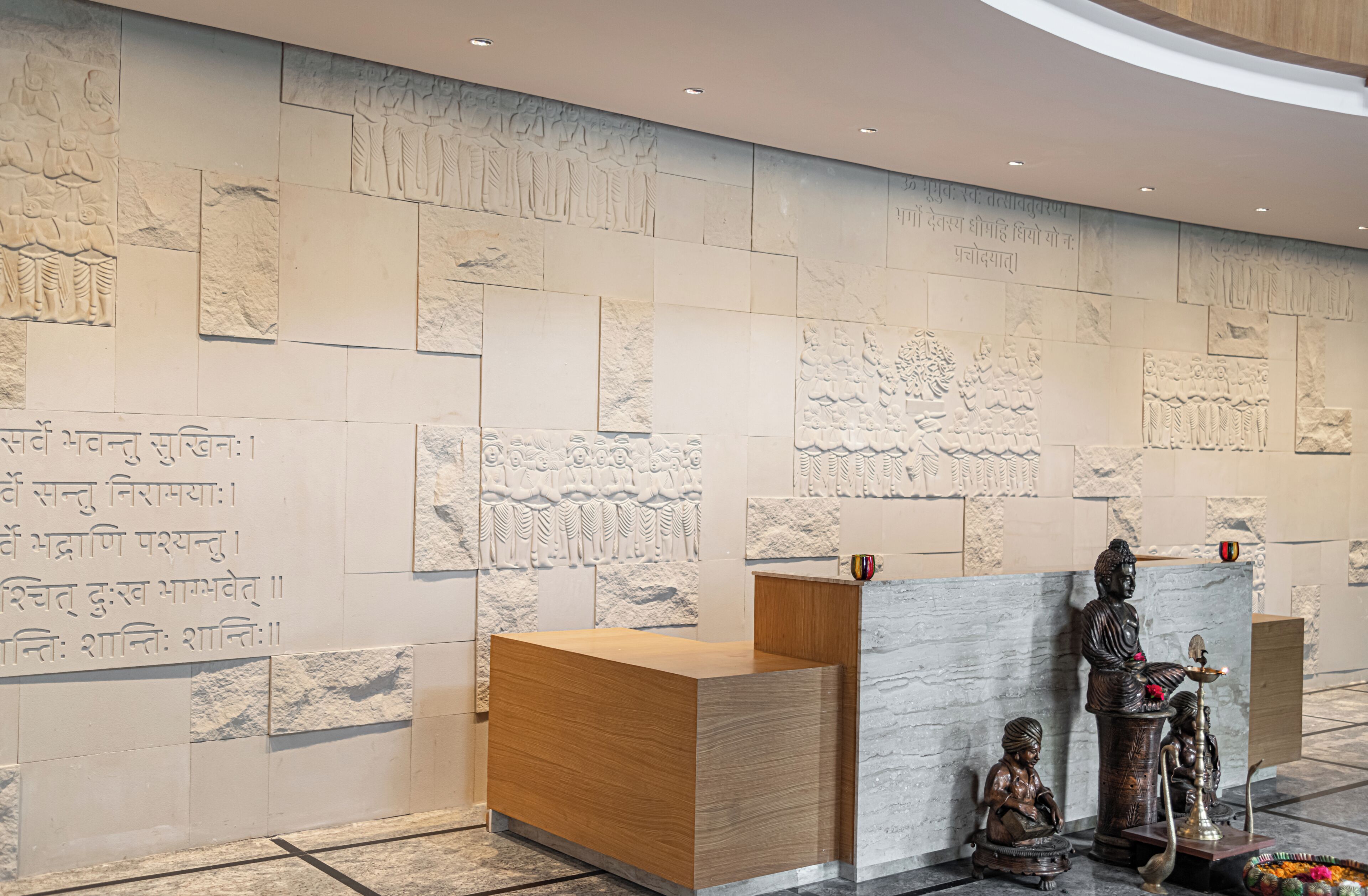 Un área de recepción con pared de mármol, mostrador de madera y una estatua de una figura sentada.