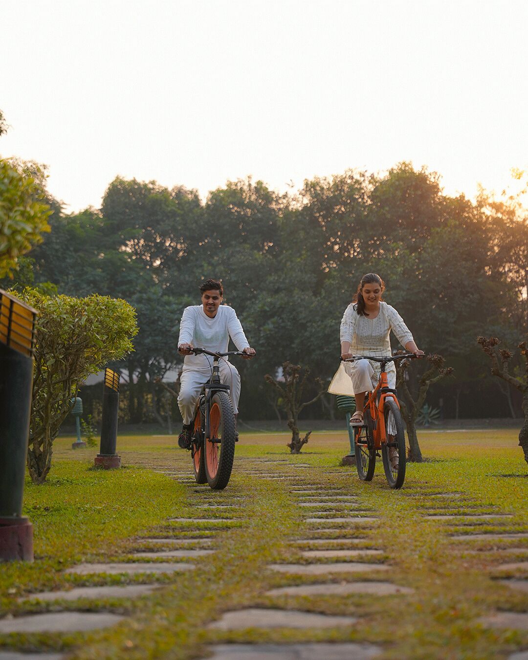 Dos personas andando en bicicleta por un camino pavimentado en un parque.