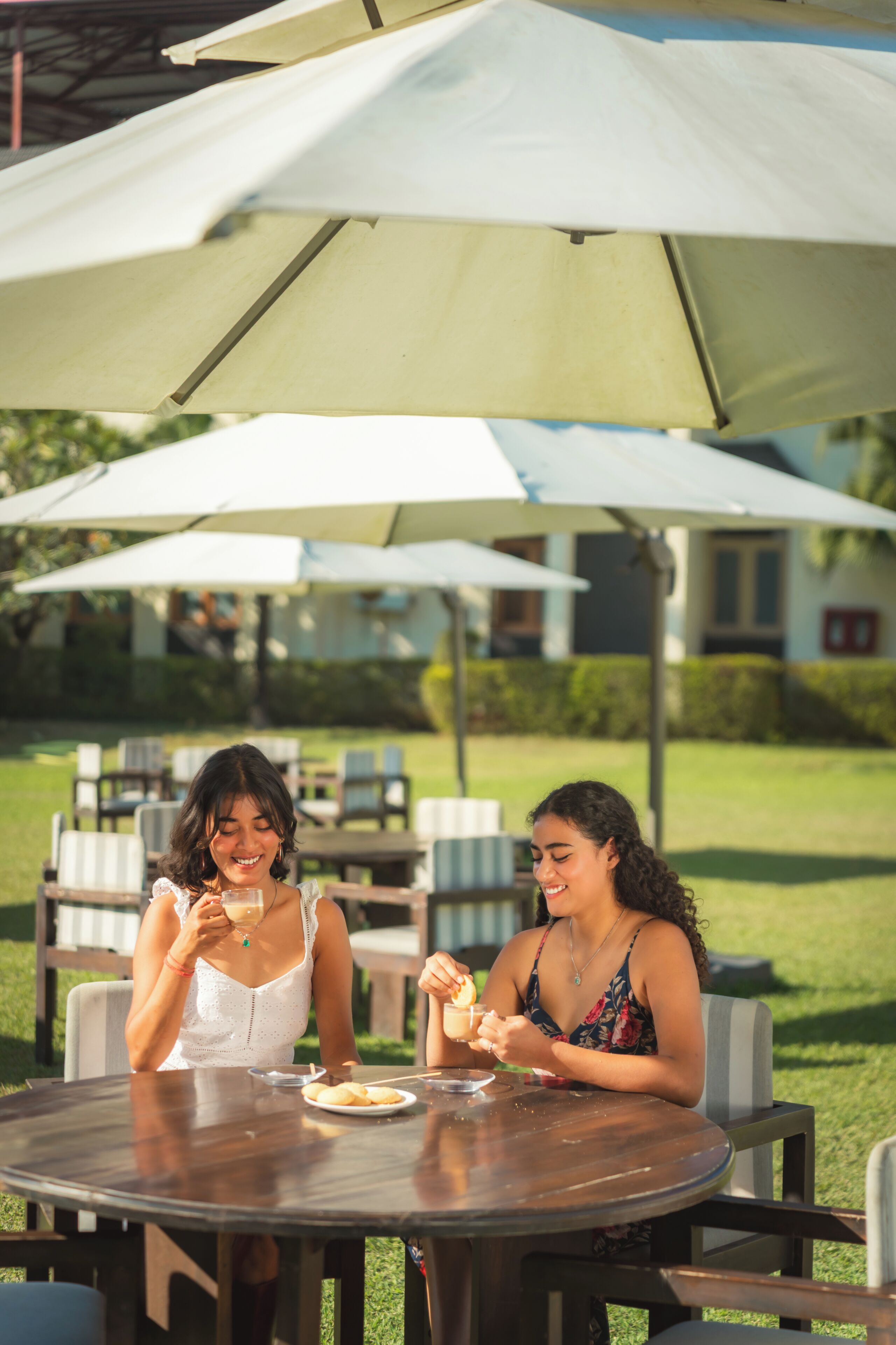 Dos personas cenando en una mesa al aire libre con sombrillas, rodeadas de sillas y una zona ajardinada.