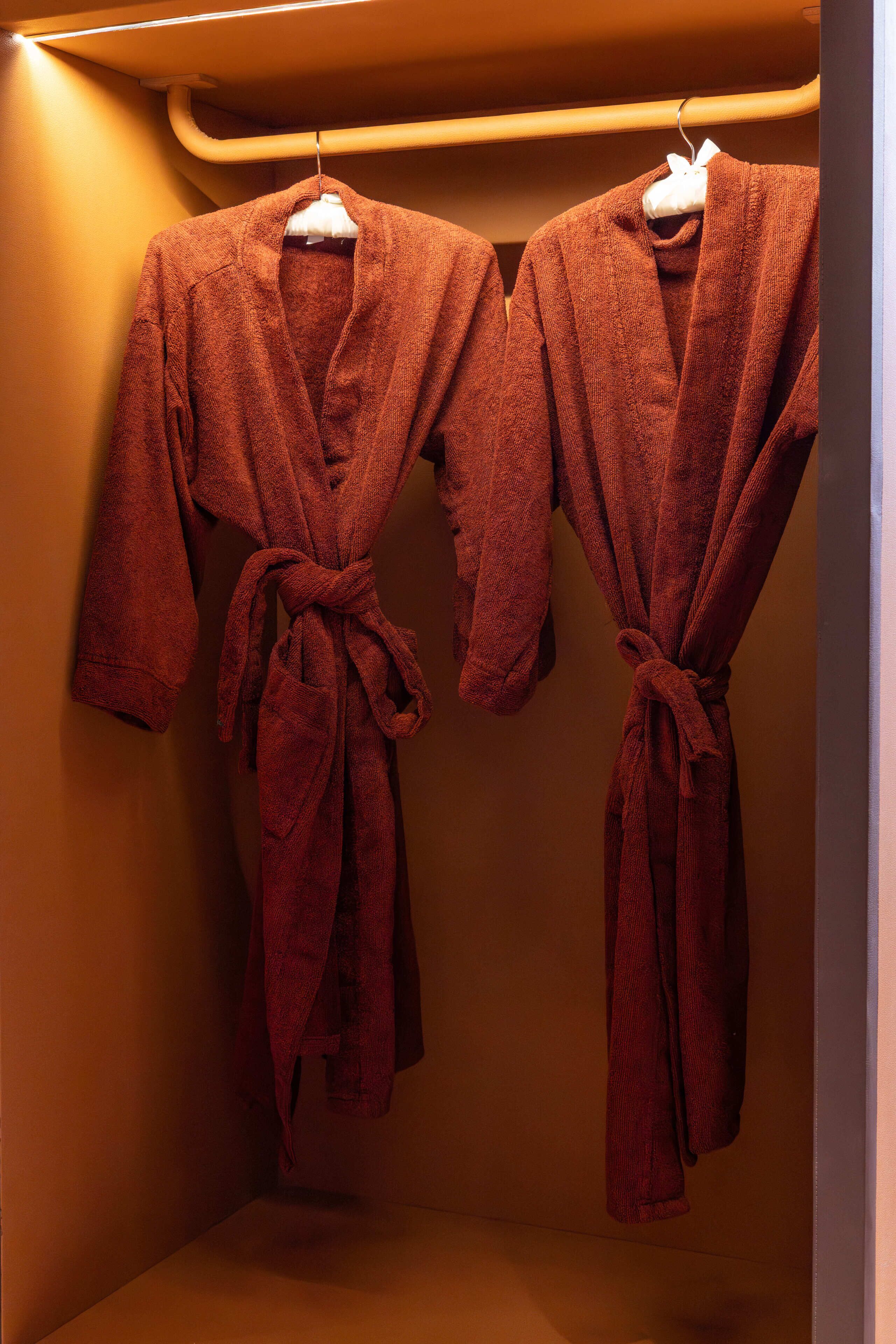 Two red bathrobes hanging on a rack in a room with a warm color scheme.