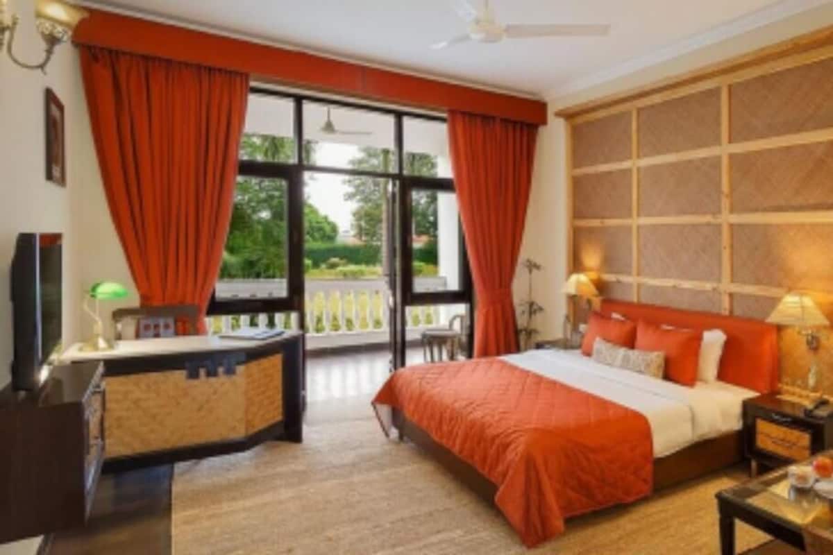 Une chambre d’hôtel avec un grand lit, un bureau, une chaise et un balcon avec des rideaux.