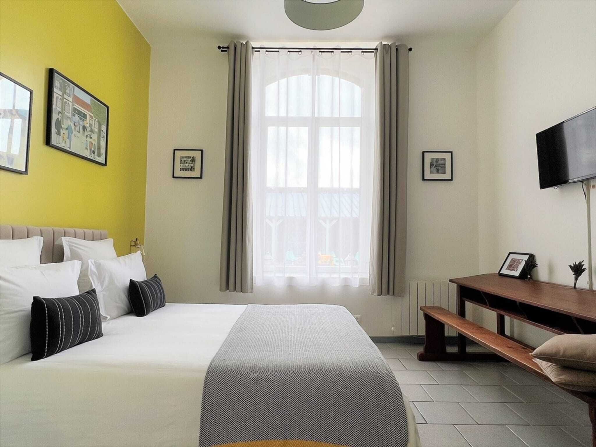 A hotel room with a bed, a desk, a television, and a window with curtains.