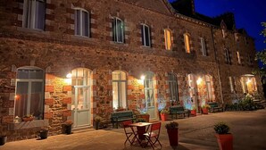 A stone building with multiple windows and doors, outdoor seating area with tables and chairs, and potted plants. - La Récréation - 1 bedroom apartment La Marelle - Covered outdoor swimming pool (Châtelaudren-Plouagat)