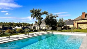 A clear blue swimming pool with lounge chairs and a stone building in the background. - La Récréation - 1 bedroom apartment La Marelle - Covered outdoor swimming pool (Châtelaudren-Plouagat)