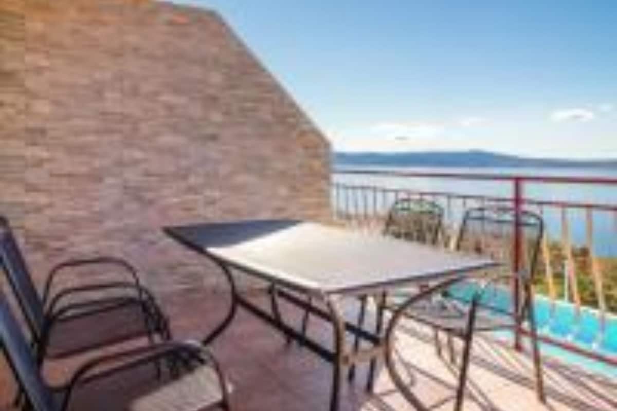 A terrace with a table and chairs, overlooking a body of water and mountains.