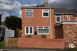 A two-story brick house with white-framed windows, a visible chimney, and a wooden fence. - Modern Interior | 5 Mins to Metro Centre | WiFi (Newcastle Upon Tyne)