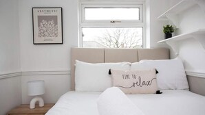 A minimalist bedroom with a bed, a framed picture on the wall, a bedside lamp, and a window. - Free Parking | 5 Min to Metro Centre | Modern House (Newcastle Upon Tyne)