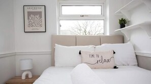 A minimalist bedroom with a bed, a framed picture on the wall, a bedside lamp, and a window. - Modern Interior | 5 Mins to Metro Centre | WiFi (Newcastle Upon Tyne)