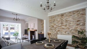 A dining area with a modern table set for four, a chandelier, and a brick-patterned wall. - Free Parking | 5 Min to Metro Centre | Modern House (Newcastle Upon Tyne)