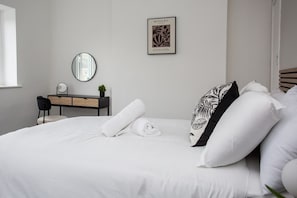 A modern bedroom with a bed, a dresser, a mirror, and a framed picture on the wall.