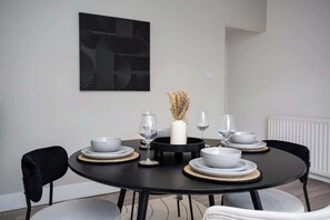 A dining area with a round table, black chairs, white plates, and a black abstract painting on the wall.