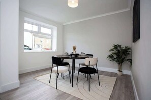 A dining area with a round table, four chairs, a potted plant, and a window with a view of the outside.