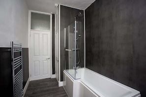 A bathroom with a bathtub, a shower enclosure, a towel rack, and a door.