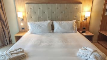 Een hotelkamer met een groot bed, twee kussens, twee bedlampen, een houten hoofdbord en twee handdoeken op het bed.