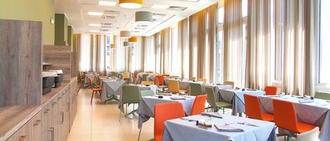 A dining area with tables and chairs, large windows, and a wooden counter.