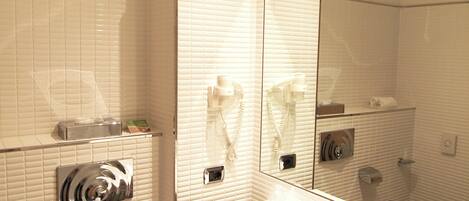 Un baño moderno con azulejos blancos, un espejo grande, un lavamanos y un inodoro.