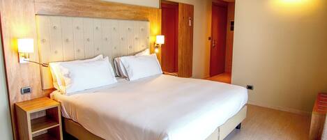 A hotel room with a large bed, wooden headboard, bedside tables, and wall-mounted lights.