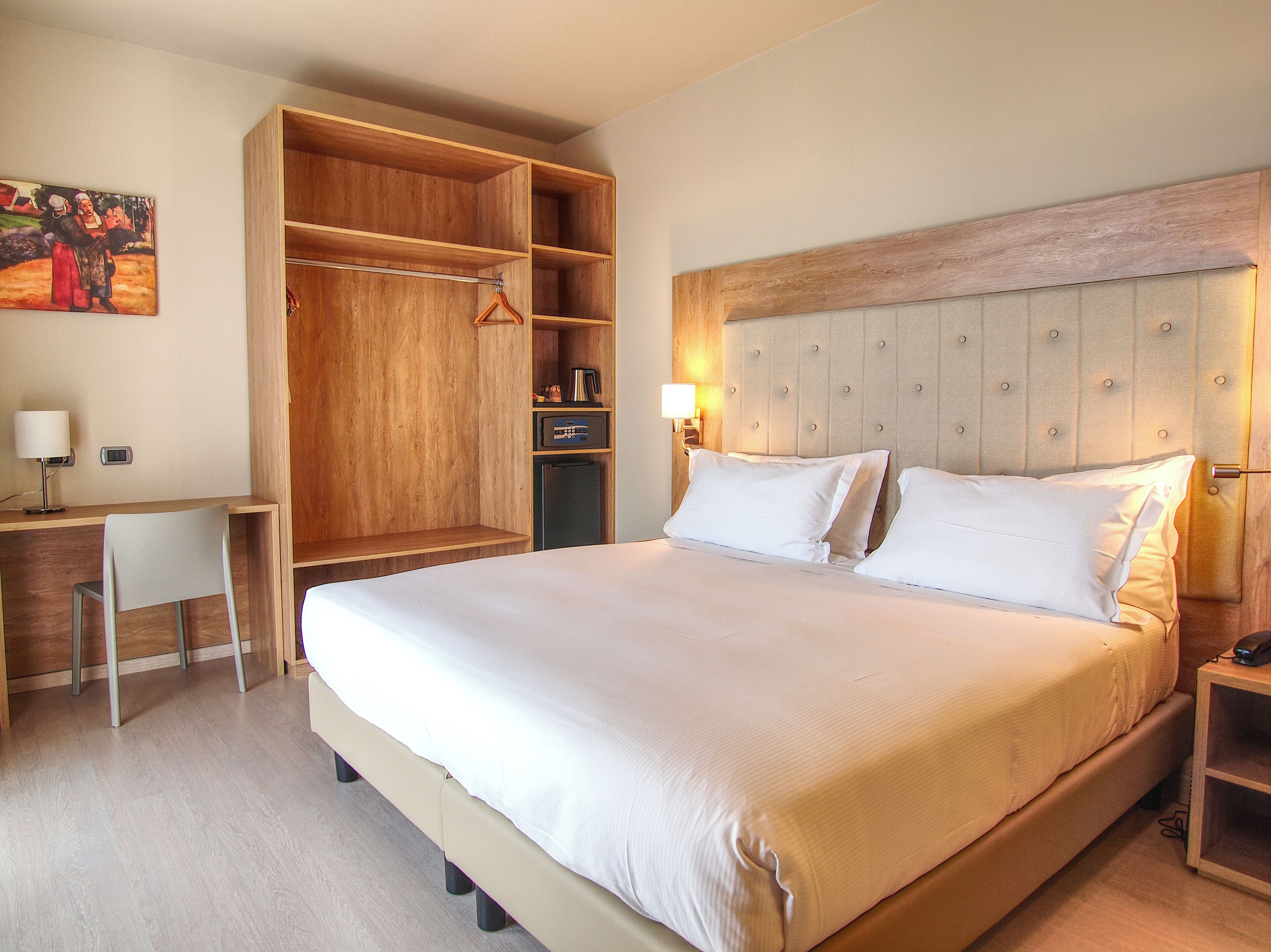 A bedroom with a large bed, a wooden wardrobe, a desk, and a chair.