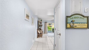 Ein Flur mit Fliesenboden, einer Tür mit dem Schild 'OUR BEACH HOUSE' und Blick auf einen Balkon mit Stuhl und Tisch.