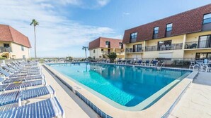 Ein rechteckiger Pool mit Liegestühlen und ein Gebäude mit Balkonen im Hintergrund.