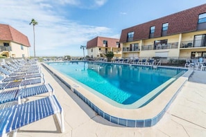 Una piscina rectangular amb gandules i un solàrium emblat, envoltada d'edificis d'alguns pisos amb balcons.