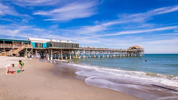 Ein Strand mit einer Pier, die sich ins Wasser erstreckt, mit einem Restaurant und einem schattigen Bereich.
