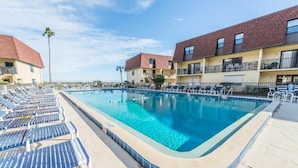 Ein rechteckiger Pool mit Liegestühlen und ein Gebäude mit Balkonen im Hintergrund.