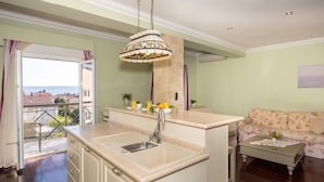 A kitchen with a large island, a dining area with a floral sofa, and a view of the outdoors. - Villa Vinovo 3 En-suite Bedroom Apartment (Kastela)