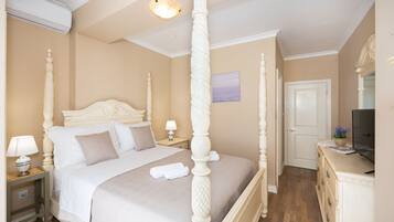A four-poster bed with a headboard, a bedside table with a lamp, and a dresser with a flat-screen TV.