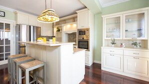 A kitchen with white cabinetry, a central island, stainless steel appliances, and a hanging chandelier. - Villa Vinovo 3 En-suite Bedroom Apartment (Kastela)