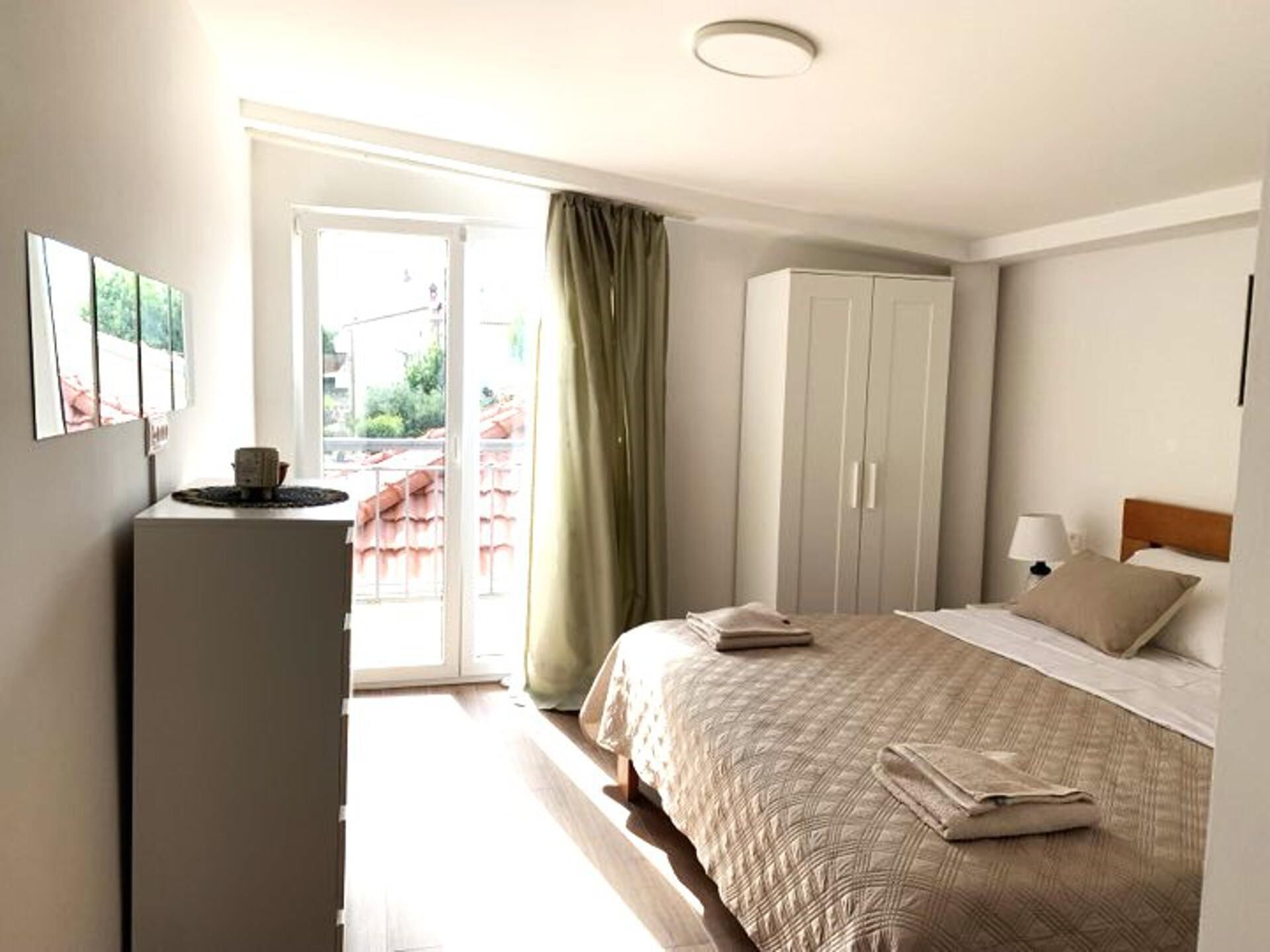 Hotellihuone, jossa on sänky, vaatekaappi, työpöytä lampun kanssa ja näkymä liukuoven kautta.