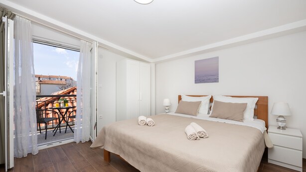 A hotel room with a bed, bedside tables, a view through a sliding door to an outdoor area with a table and chairs. - Lovely 1 Bedroom Apartment (Kastela)