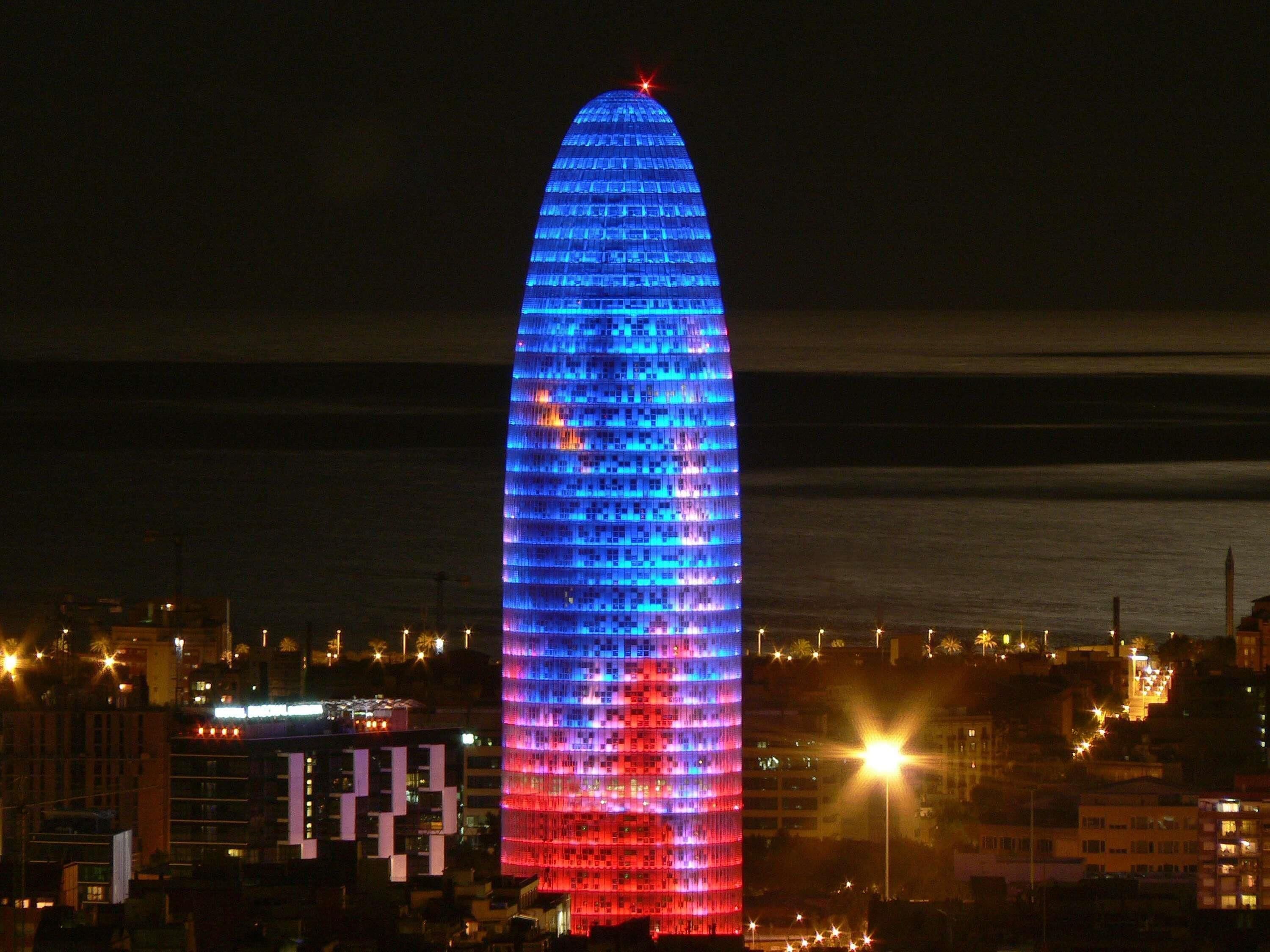 A tall, illuminated building with a pointed top, surrounded by other buildings.