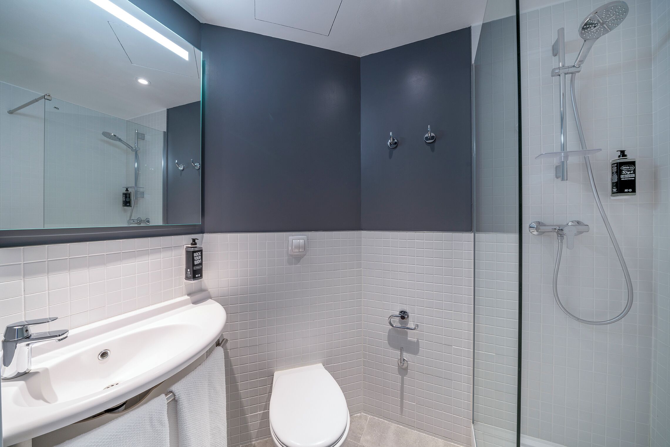 Un baño moderno con un lavamanos blanco, un inodoro y una zona de ducha.