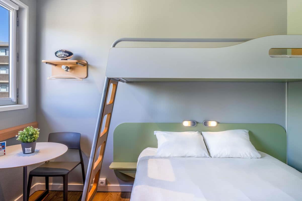 Un lit superposé avec une échelle, une petite table avec une plante et une chaise dans une pièce avec une fenêtre.