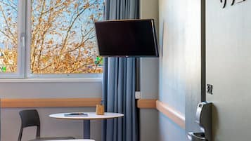 A hotel room with a bed, a desk, a television mounted on the wall, and a suitcase on the floor.