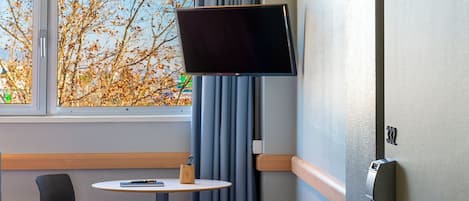 A hotel room with a bed, a desk, a television mounted on the wall, and a suitcase on the floor.