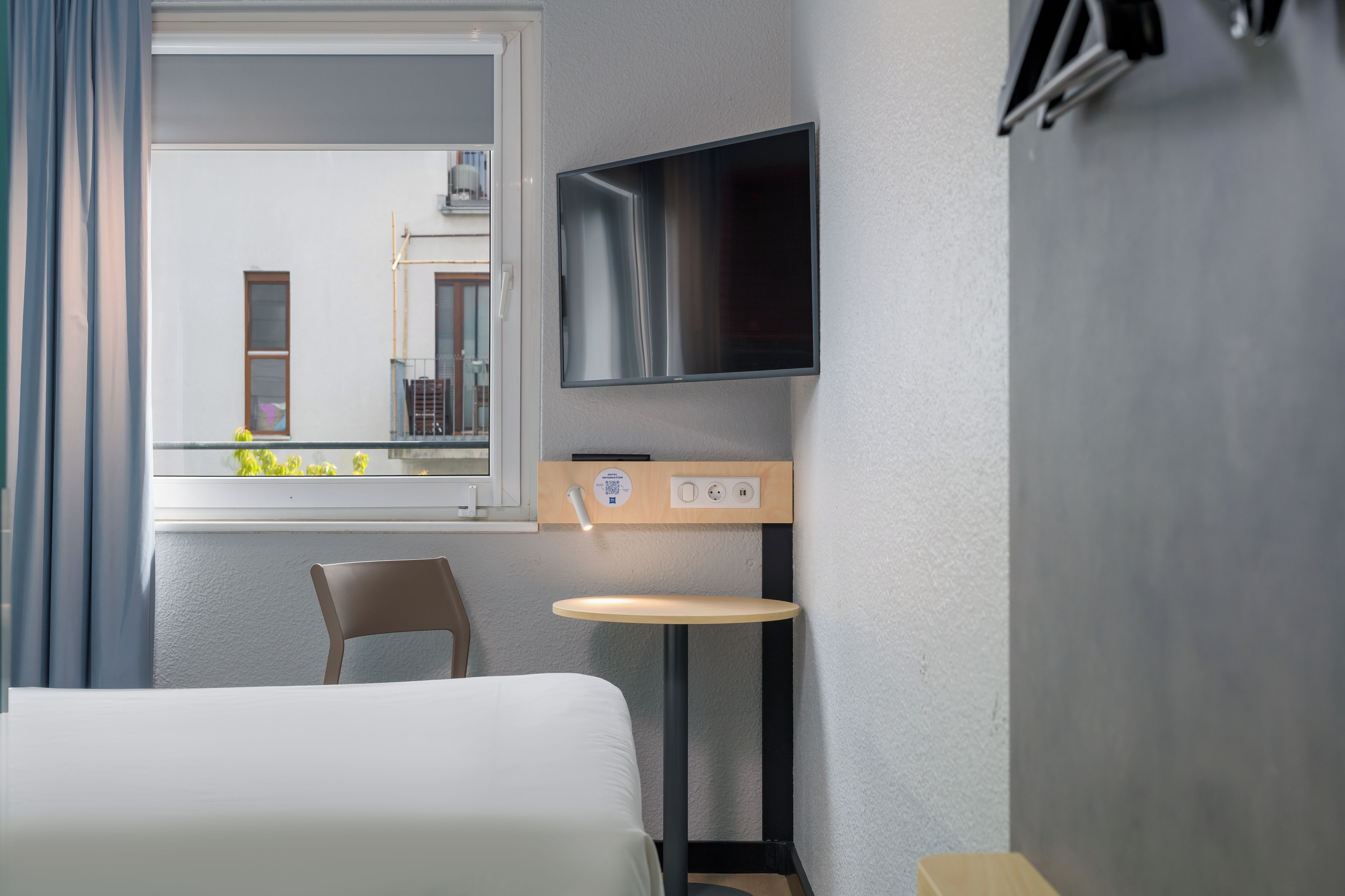 A hotel room with a bed, a television, a small table, and a chair.