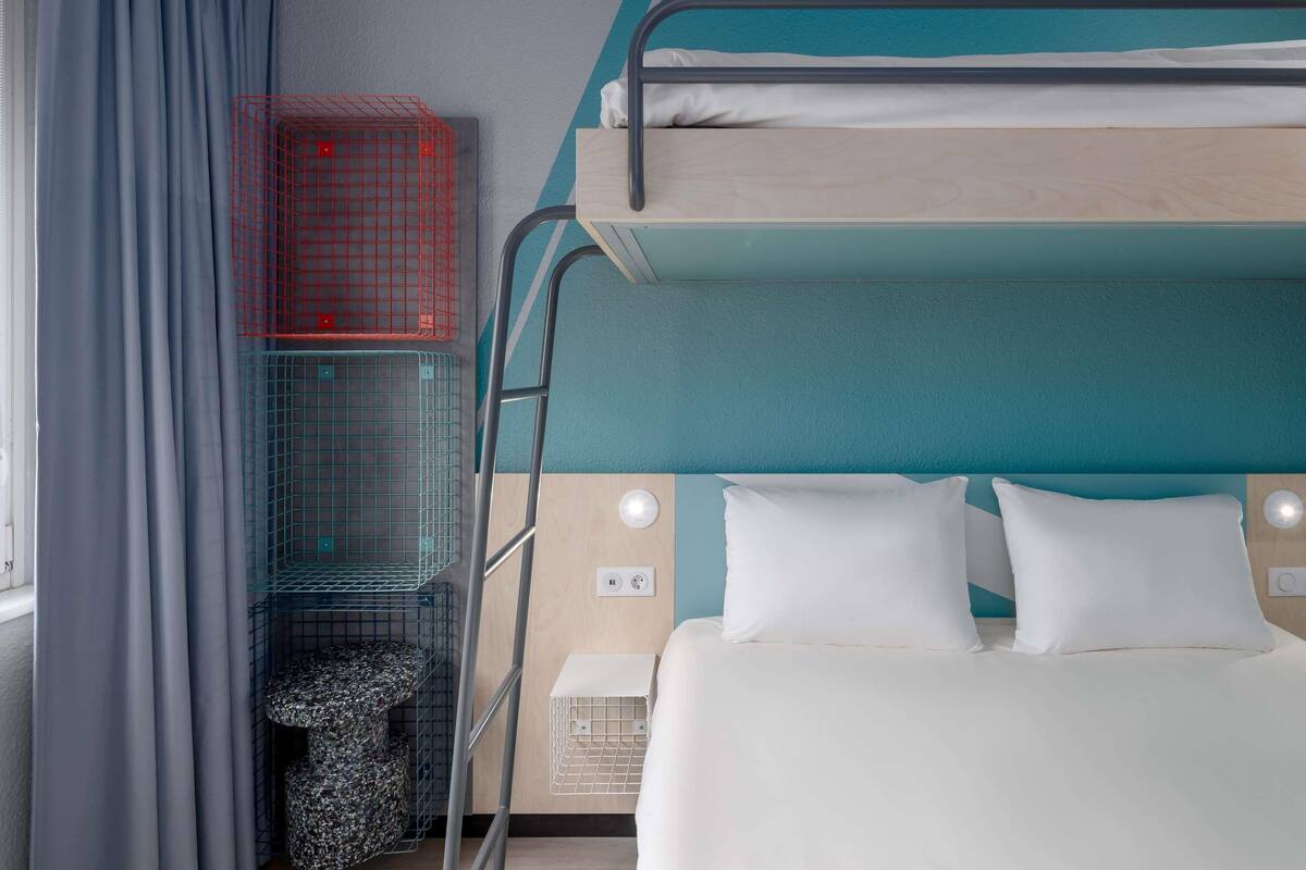 Dormitorio con literas, ventana, cortinas y una mesita pequeña.