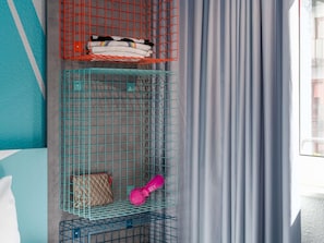 Una habitación con pared verde azulado, una ventana con cortinas grises y una estantería metálica con varios objetos.