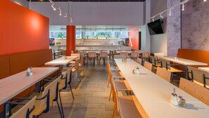 Ein modernes Restaurant mit langen Tischen, Stühlen und einer Küche im Hintergrund.