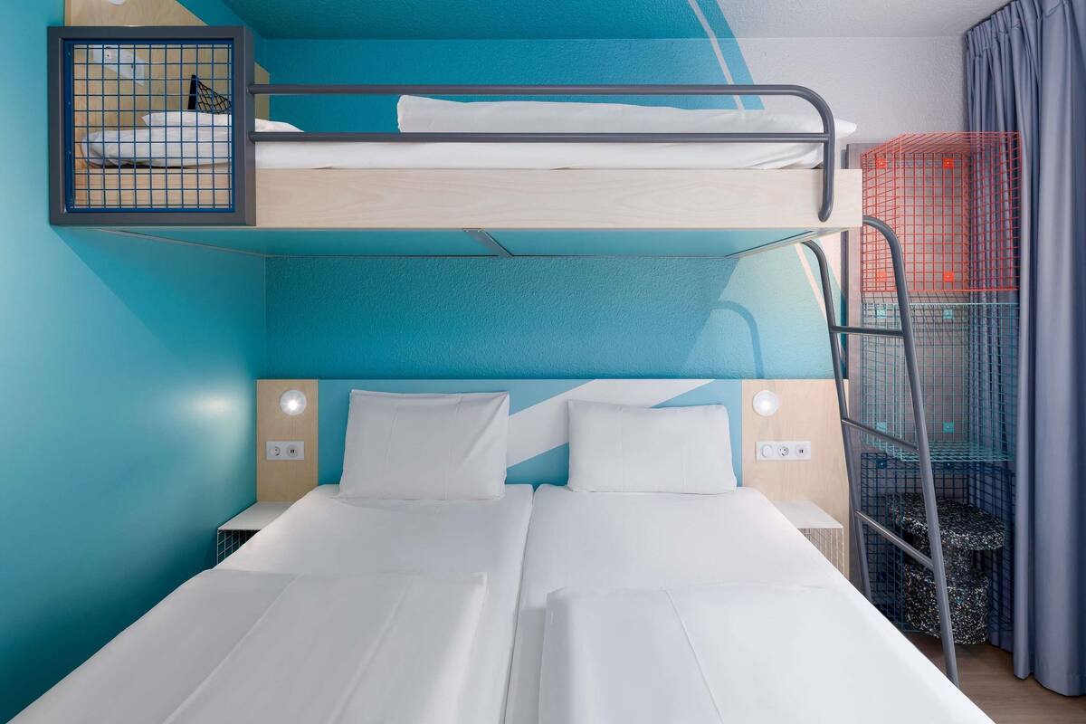 Habitación con literas, una cama inferior, cabecera y mesita de noche con lámpara.