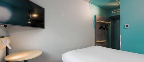 A hotel room with a bed, a TV mounted on the wall, a small round table, and a mirror.