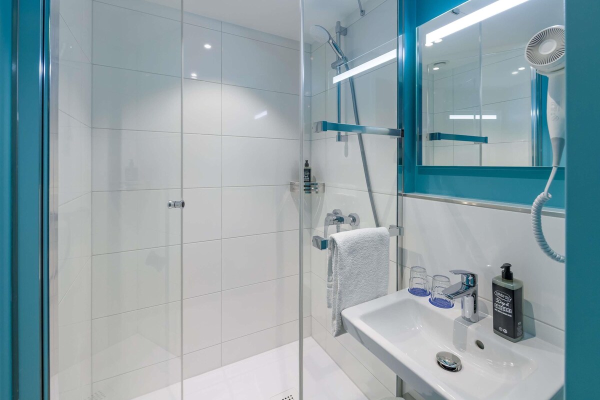 Ein modernes Badezimmer mit Duschkabine aus Glas, einem weißen Waschbecken und einem Spiegel sowie einer Handbrause.