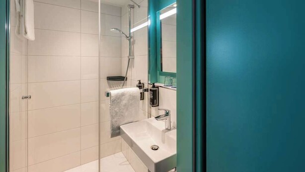 Un baño moderno con cabina de ducha de vidrio, un lavamanos blanco y una pared de acento color aguamarina.
